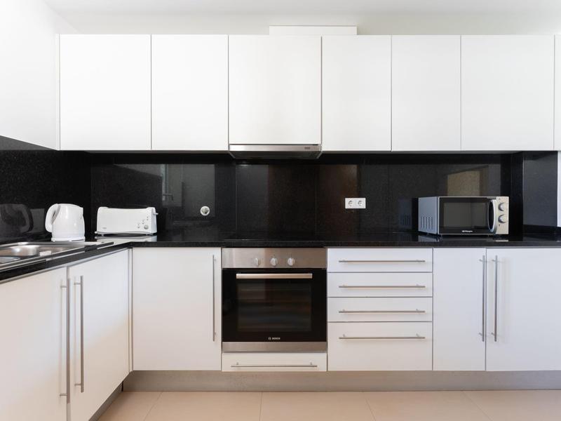 Moderne Hotelküche mit weißen Schränken, schwarzen Arbeitsflächen und Geräten wie Ofen und Mikrowelle.