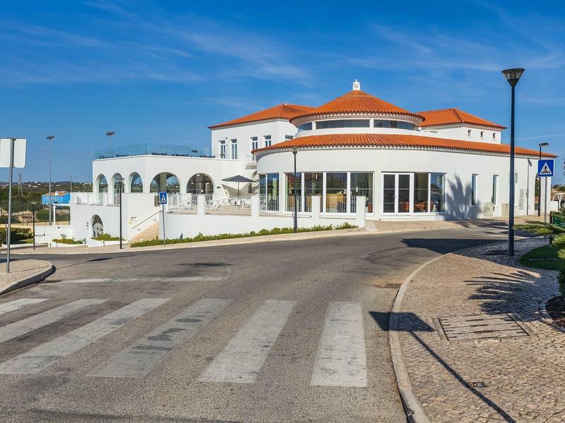 Rundes weißes Gebäude mit rotem Dach an einer Straße, klarer blauer Himmel, Laternen und Gehweg.