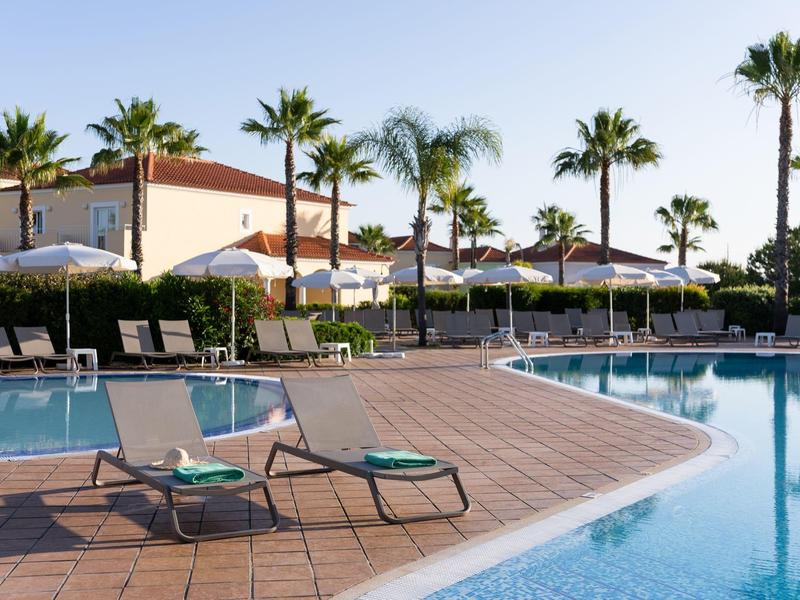 Moderner Poolbereich mit Liegestühlen, Sonnenschirmen, Palmen und angrenzendem Haus bei klarem Himmel.