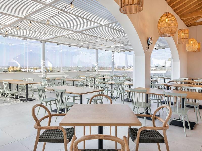 Helle, offene Dachterrassen-Gastronomie mit weißen Tischen, Stühlen und Cityblick bei Tageslicht.