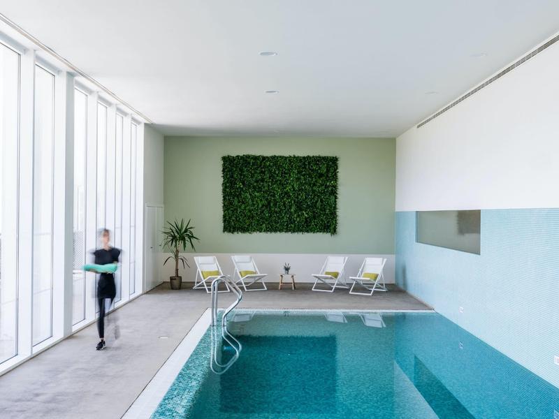Moderner Innenpool mit grünem Pflanzenbild, Liegstühlen und großen Fensterfronten.