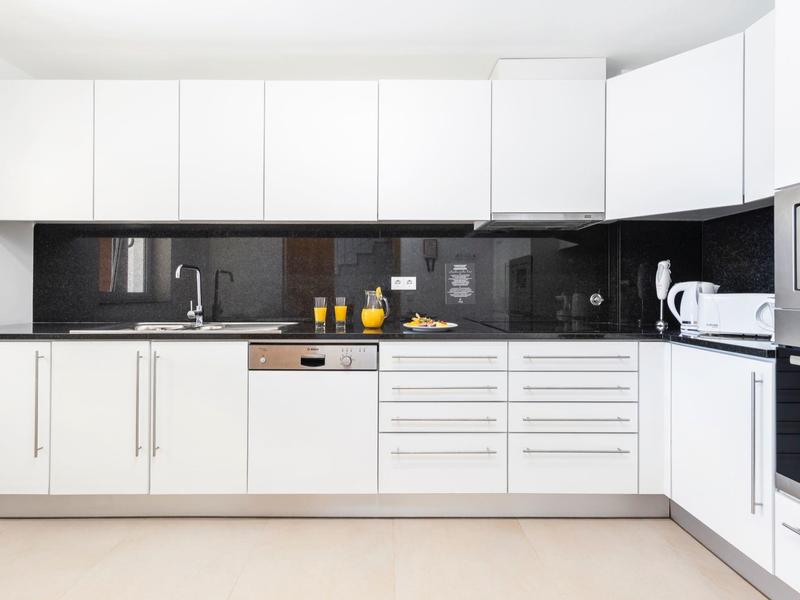 Moderne weiße Küche mit schwarzen Arbeitsflächen, integriertem Geschirrspüler und eingebauten Geräten.