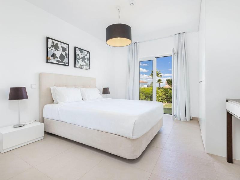 Helles Schlafzimmer mit großem Bett, weißen Möbeln, zwei Schwarz-Weiß-Bildern und Balkon mit Meerblick.