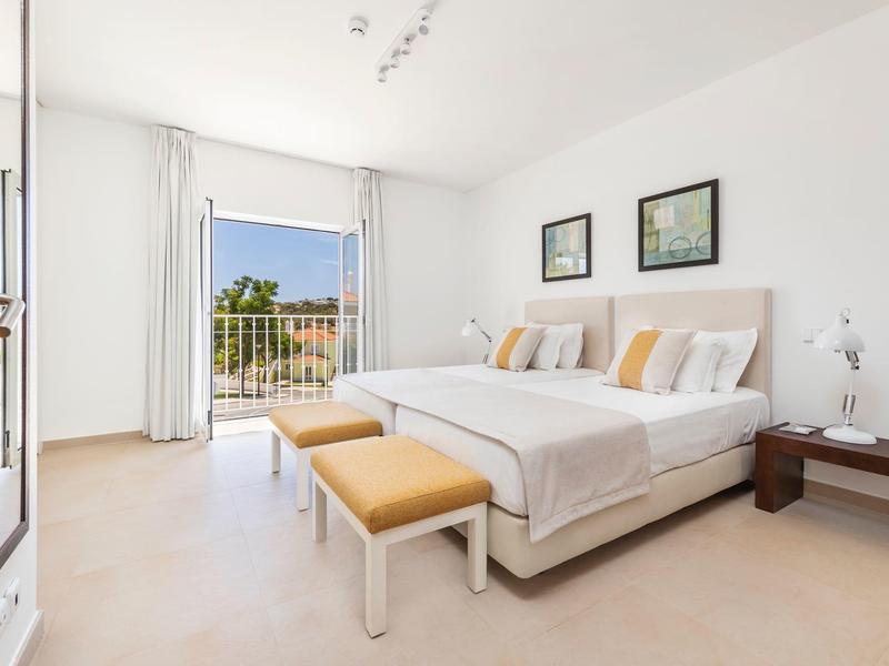 Hell eingerichtetes Schlafzimmer mit großem Bett, weißen Wänden und Balkon mit Aussicht.