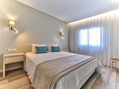 Helles Schlafzimmer mit großem Bett, zwei blauen Kissen, Nachttischen und weichen Vorhängen.