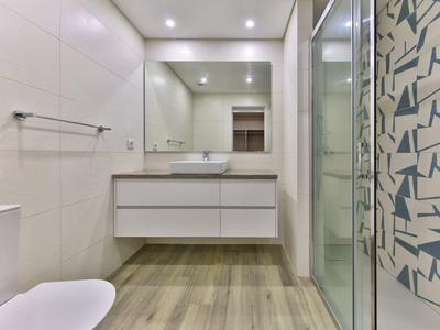 Helles, modernes Badezimmer mit Holzfußboden, weißem Waschbecken und Duschnische mit gemusterten Fliesen.