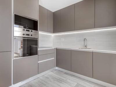 Moderne Küche mit grauen Schränken, eingebauten Edelstahlgeräten und hellgrauem Fliesenboden.