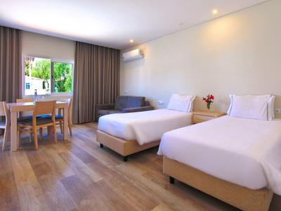 Helles Zimmer mit zwei Einzelbetten, Holzfußboden, Esstisch und Fenster mit Blick ins Grüne.