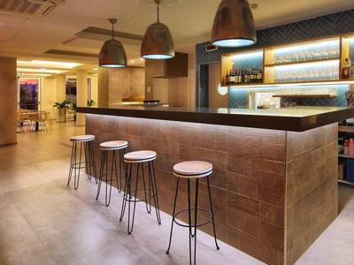 Moderner Barbereich mit Stehtischen, vier Hockern und drei überhängenden Metalllampen.