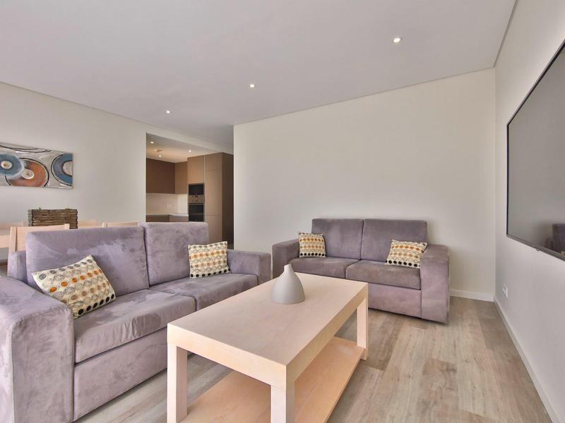 Modernes Wohnzimmer mit zwei grauen Sofas, hellem Holztisch und großem wandmontiertem Fernseher.