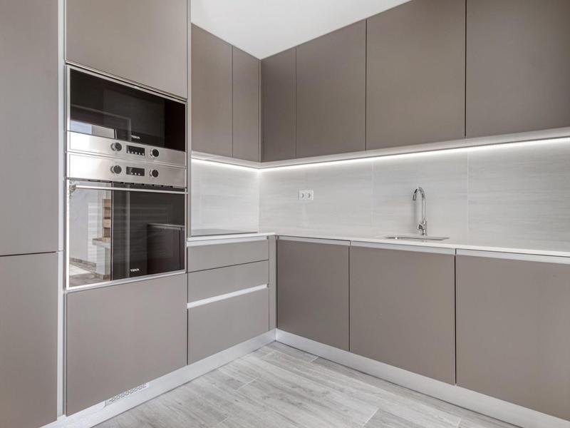 Moderne Küche mit grauen Schränken, eingebauten Edelstahlgeräten und hellgrauem Fliesenboden.