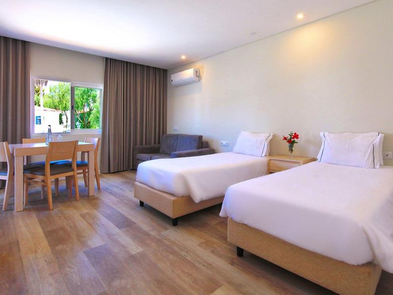 Helles Zimmer mit zwei Einzelbetten, Holzfußboden, Esstisch und Fenster mit Blick ins Grüne.