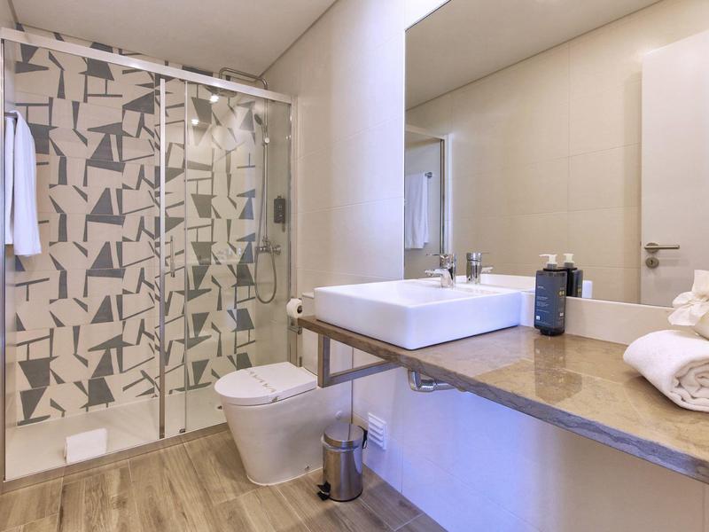 Modernes Badezimmer mit Dusche, weißem Waschbecken, großem Spiegel und Holzboden.