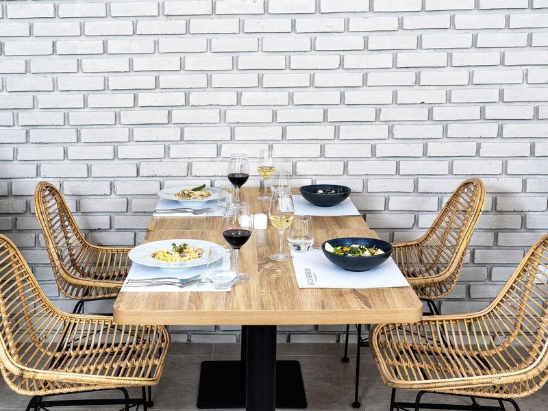 Moderner Holztisch mit sechs geflochtenen Korbstühlen, gedeckt mit Tellern, Gläsern und Besteck.