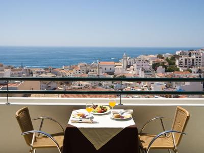 Tisch mit Frühstück auf Balkon mit Blick auf Küstenstadt und Meer.