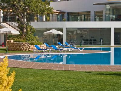 Moderner Poolbereich mit Liegestühlen und Sonnenschirmen vor einem Hotelgebäude.