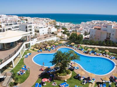 Hotelanlage mit unregelmäßig geformtem Pool, umgeben von Liegestühlen und Meerblick.