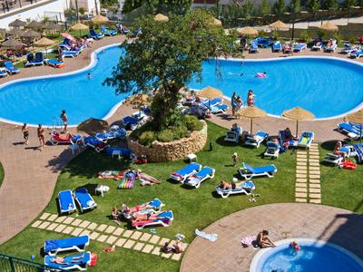 Hotelaußenpool mit unregelmäßigem Umriss, umgeben von Liegestühlen und Sonnenschirmen auf Rasen.