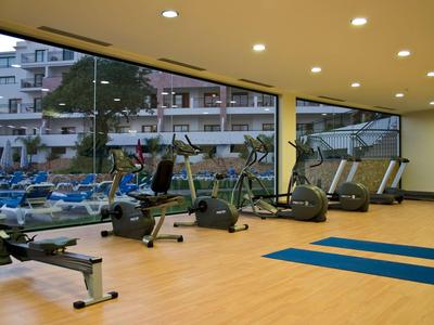 Fitnessraum mit modernen Geräten und großen Fenstern mit Blick auf eine Außenanlage.