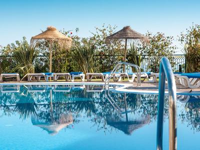 Klare blaue Poolwasserfläche mit Liegestühlen und Sonnenschirmen unter blauem Himmel.