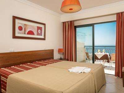 Hotelzimmer mit Doppelbett, Balkon und Meerblick bei klarem Wetter.