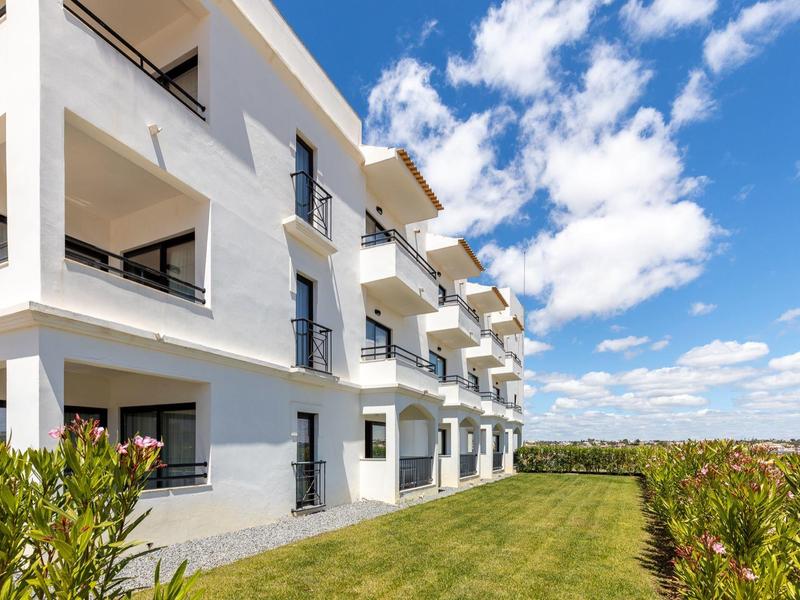 Moderner weißer Wohnblock mit Balkonen, grünem Rasen und blauem Himmel mit Wolken.