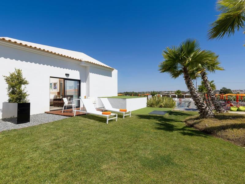 Modernes weißes Haus mit Liegestühlen, grüner Rasenfläche und Palmen bei blauem Himmel.