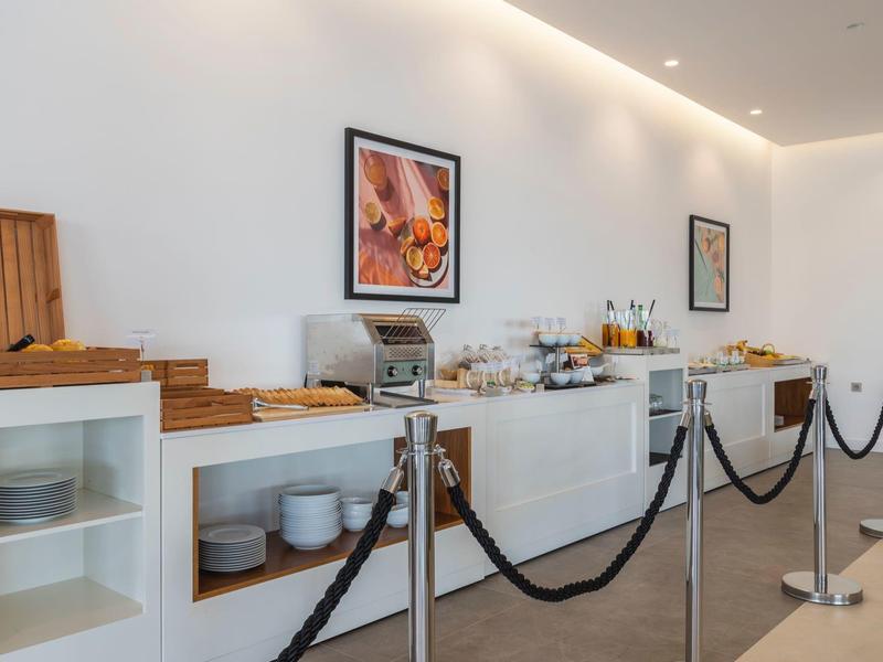 Buffetbereich mit weißem Mobiliar, Gläsern, Tellern, Brotkorb und Kunst an der Wand.