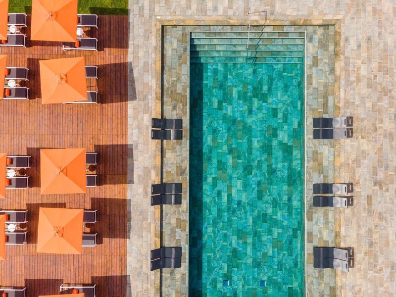 Symmetrisches Schwimmbad mit türkisfarbenem Wasser, umgeben von Holzboden und orangen Sonnenschirmen.