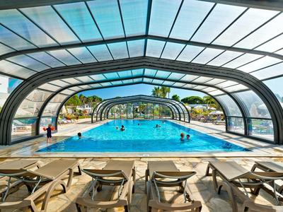 Überdachtes Schwimmbad mit Liegestühlen und Blick auf den sonnigen Außenbereich.