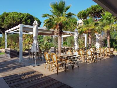 Freiluftrestaurant mit Tischen, Stühlen und Palmen bei sonnigem Wetter