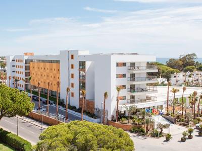 Moderner mehrstöckiger Hotelkomplex mit weißer und holzfarbener Fassade, umgeben von Bäumen.