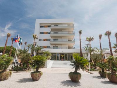 Modernes Hotel mit mehreren Stockwerken, umgeben von Palmen und tropischer Vegetation.
