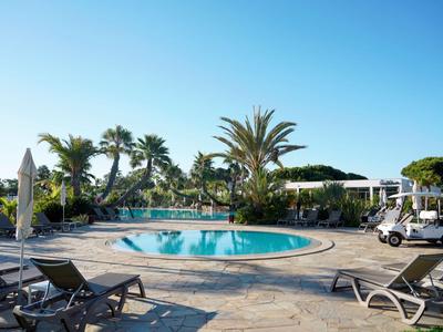 Rundes Schwimmbecken mit Liegestühlen und Palmenschirmen im sonnigen Hotelgarten.