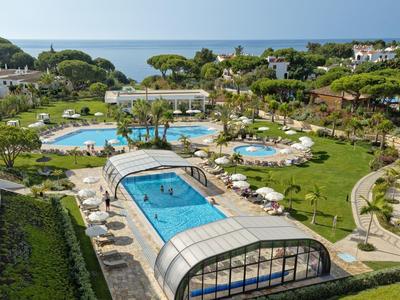 Großer Hotelpool mit überdachtem Bereich, umgeben von Liegestühlen und grünen Gärten nahe dem Meer.