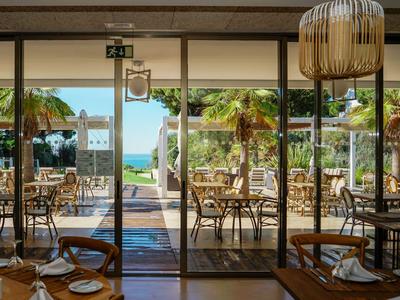 Blick durch ein Restaurant mit gedeckten Tischen auf eine Terrasse mit Palmen und Meerblick.