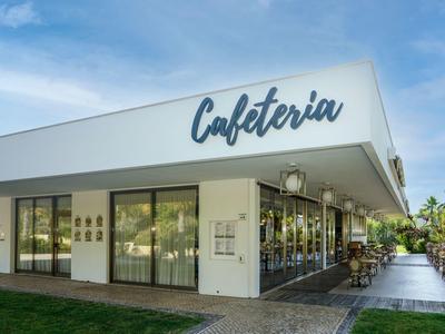 Modernes Cafeteria-Gebäude mit großflächigen Fenstern und Außenbestuhlung unter blauem Himmel.