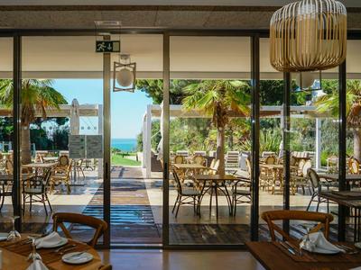 Blick durch ein Restaurant mit Holzmöbeln und Blick auf Terrasse und Meer im Hintergrund.