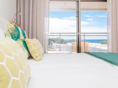 Helles Schlafzimmer mit großen Fenstern und Meerblick, modernes Design und pastellfarbene Kissen.