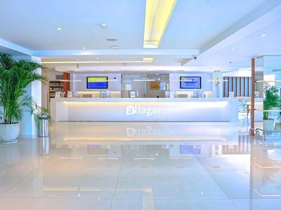 Helle, moderne Hotellobby mit glattem Boden, beleuchteter Rezeption und grünen Pflanzen.