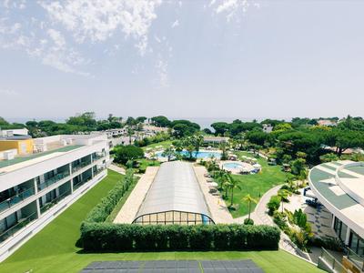 Blick auf ein Hotelgelände mit Pool, Gartenanlagen und umliegender Landschaft unter blauem Himmel.