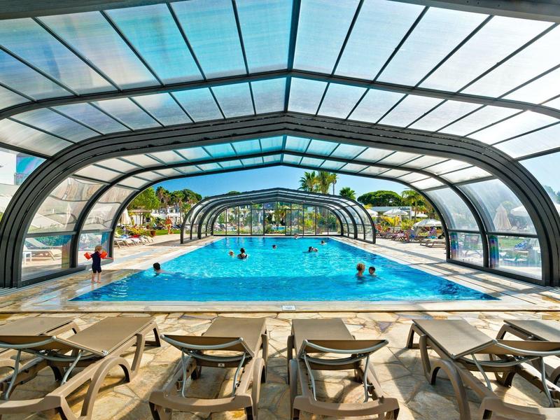 Überdachtes Schwimmbad mit Liegestühlen und Blick auf den sonnigen Außenbereich.