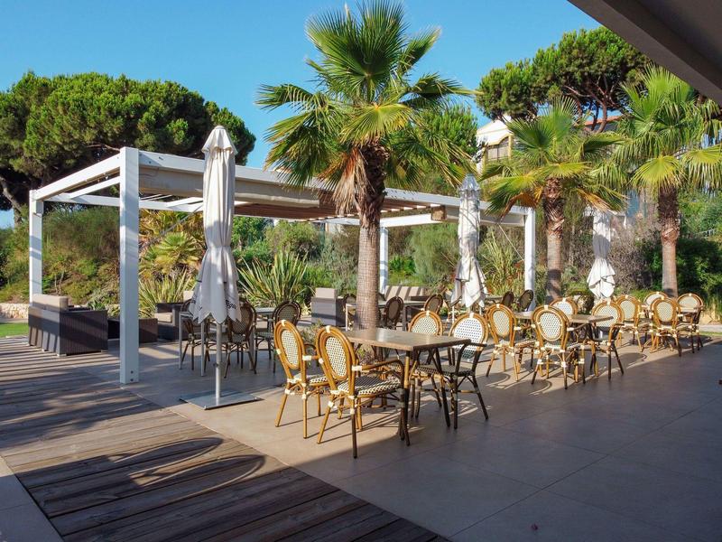 Freiluftrestaurant mit Tischen, Stühlen und Palmen bei sonnigem Wetter