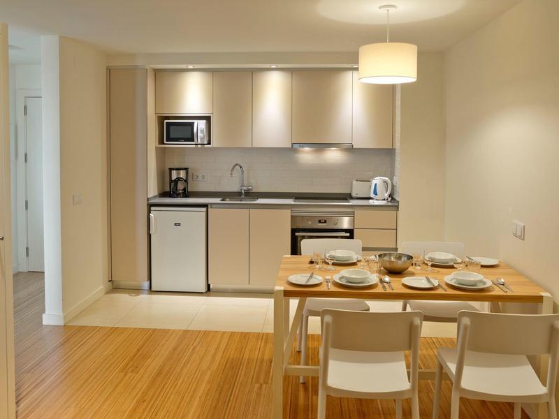 Modern eingerichtete Küchenzeile mit Esstisch und fünf Gedecken in einem Hotelzimmer.