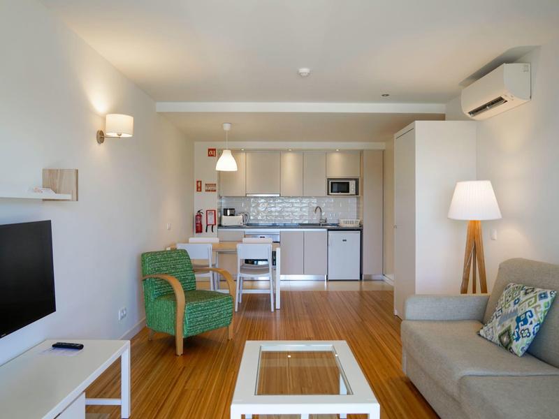 Moderner Wohnbereich mit Sofa, grünem Sessel und offener Küche mit Essbereich.