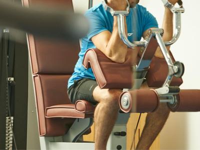 Person sitzt auf Fitnessgerät und macht Übungen mit Armen im Hotel-Fitnessraum.