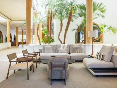 Moderne Lounge mit Sofas und Stühlen in einer offenen, hellen Hotellobby mit Palmen.
