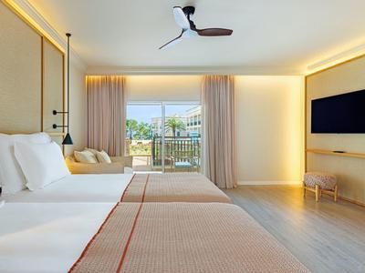 Helles Hotelzimmer mit zwei Betten und Terrasse mit Blick auf den Pool.