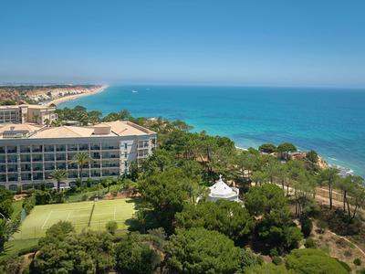 Blick auf ein Hotel am Meer mit grünen Bäumen und klarem blauem Himmel.