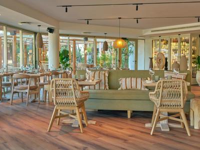 Helles Restaurant mit Holzfußboden, Stühlen aus Rattan und grünen Sofas.